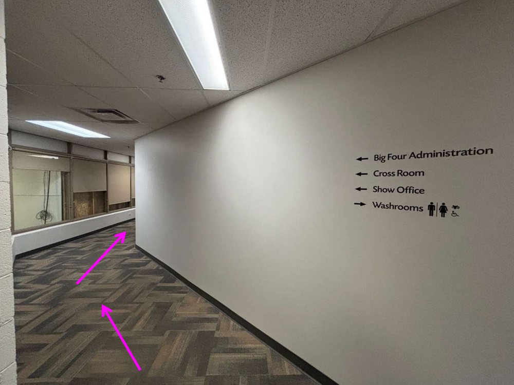 A lower-level hallway with a wall sign listing Show Office and other rooms with arrows.