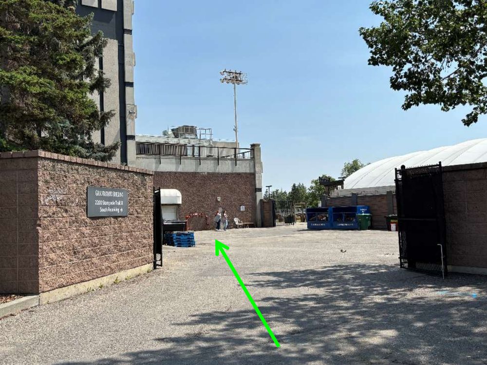 The GMC south receiving yard, with the Grandstand Building sign, an open gate, and the gravel yard leading to the employee door.